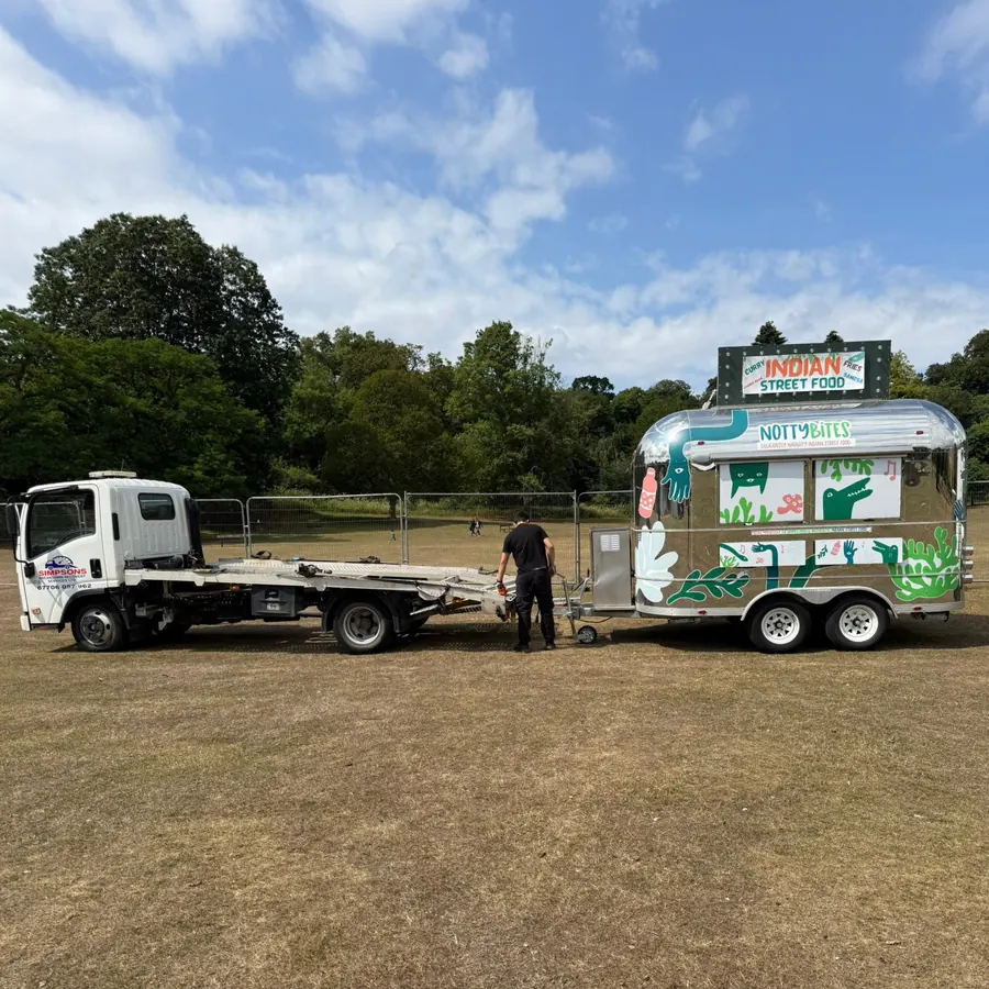 Simpsons Breakdown Recovery truck towing a NottyBites Indian street food trailer at an outdoor event site